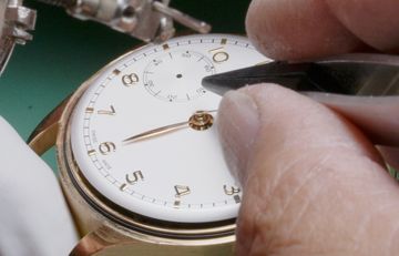 Tweezers positioned over the center of a gold watch dial during hand repair