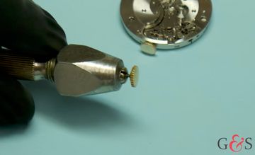 Gold watch crown held in a precision workshop tool