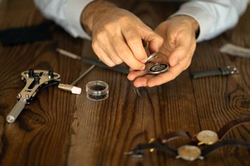 Hands opening a wristwatch case with a case knife on a wooden bench