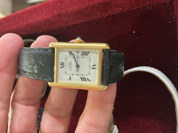 Vintage rectangular gold watch held above a red work surface