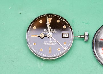 Detached watch hand beside a vintage GMT dial and exposed movement