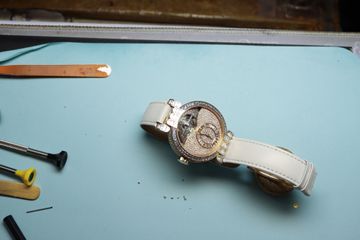 Skeleton tourbillon watch on a workshop mat beside precision tools and small components