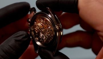 Opened chronograph movement held in black gloves for inspection