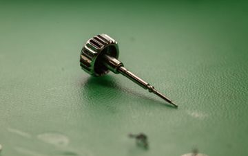 Detached watch crown and winding stem on a green work mat