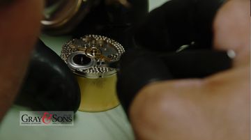 Gloved hands working on an open mechanical watch movement