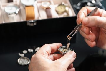 Tweezers handling a balance assembly above an open mechanical watch movement
