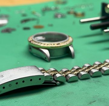 Disassembled two-tone Rolex bracelet, clasp, and watch case on a workshop mat